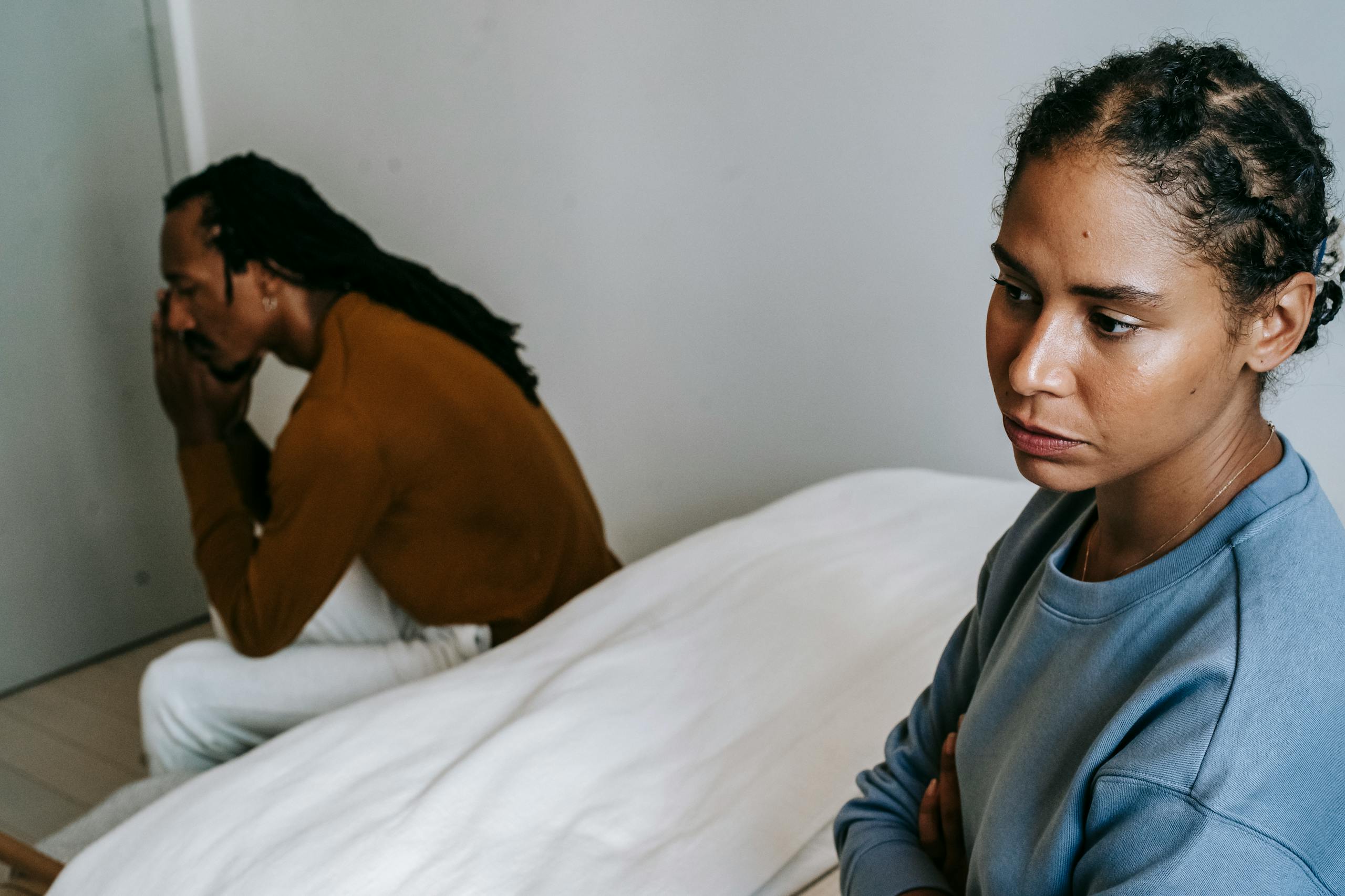 Young African American couple resting on bed and thinking while wearing casual clothes at home