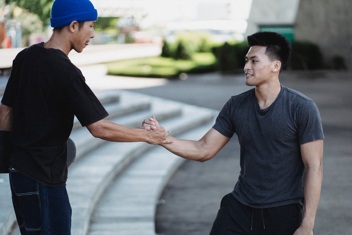 Young Asian friends in casual clothes shaking hands while standing in urban street