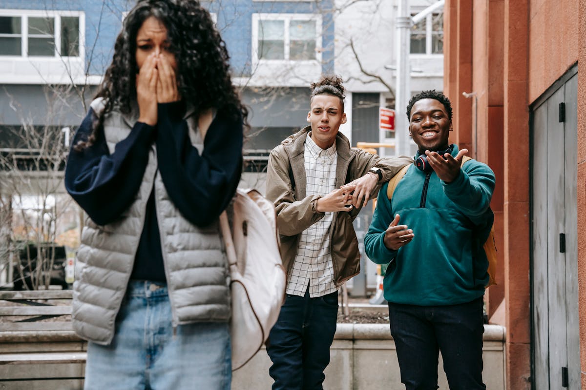 10 Warning Signs Your Friends Are Damaging Your Relationship And How You Can Protect It 2 Young multiethnic male students laughing at upset female classmate covering mouth with hands and crying on street