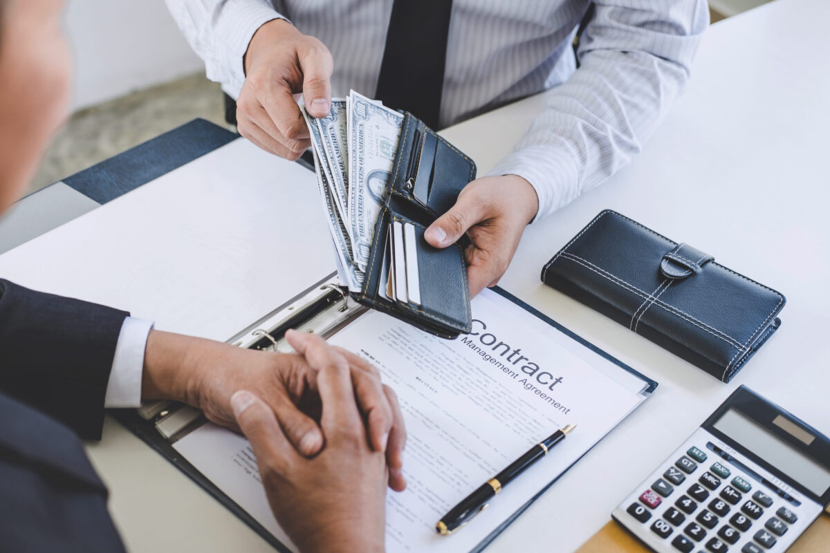 Bribery and corruption concept, bribe in the form of dollar bills, Businessman giving money while making deal to agreement a real estate contract and financial accounting.