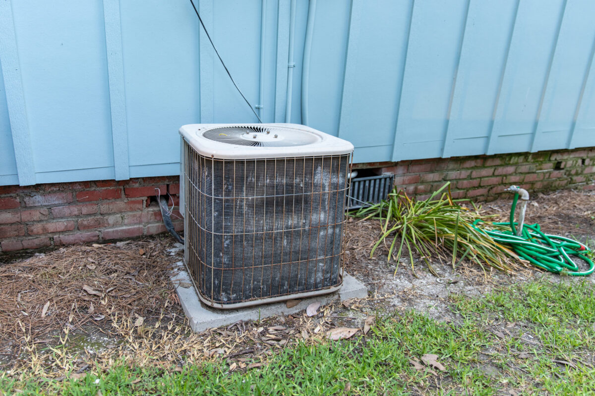Old air conditioner system compressor next to home, needing maintenance.