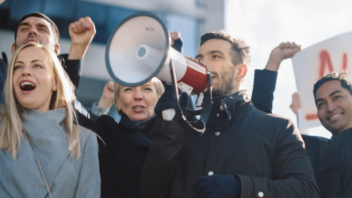 Multicultural Diverse Office Managers and Business People Picketing Outside on a Street. Men and Women Screaming for Justice, Holding a Megaphone, Picket Signs and Posters. Economic Crisis Strike.