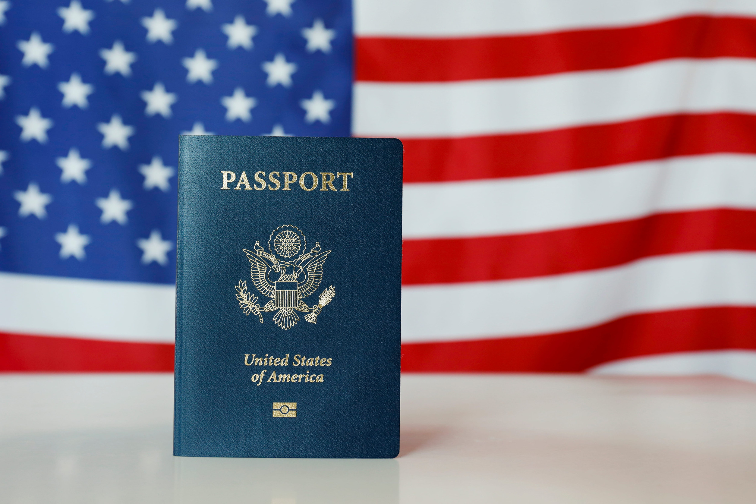 Latest version of United States of America citizen Passport with biometric ID chip standing on table with USA flag on background. Person identification document on display. Close up, copy space.