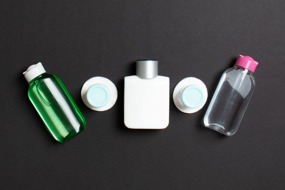 Top view of means for face care: bottles and jars of tonic, micellar cleansing water, cream, cotton pads on colored background. Bodycare concept with empty cpace for your ideas.