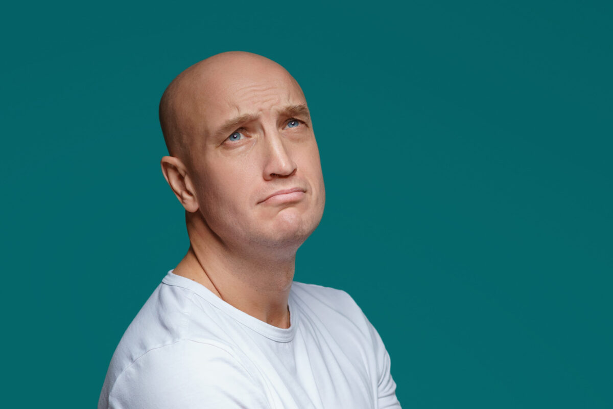 Portrait of a bald adult man with a sad expression in a white t shirt on a blue background.