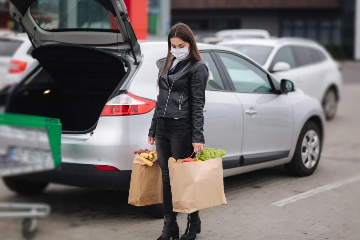 Groceries from a supermarket in a eco craft package. Food delivery during quarantine. Paper eco bags full of fresh food. Woman hold two package by the car