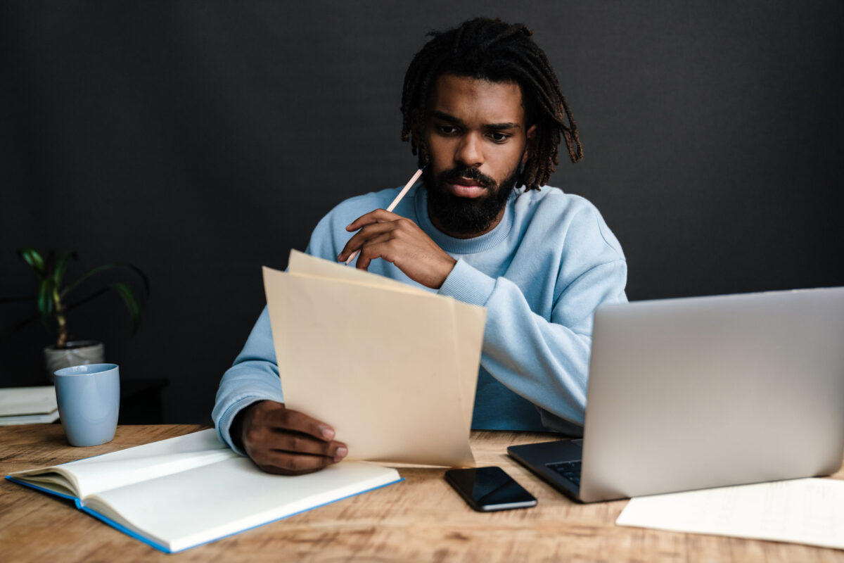 Handsome serious young african man sitting at a coffee shop with pensive look, thinking of business plans, working on laptop