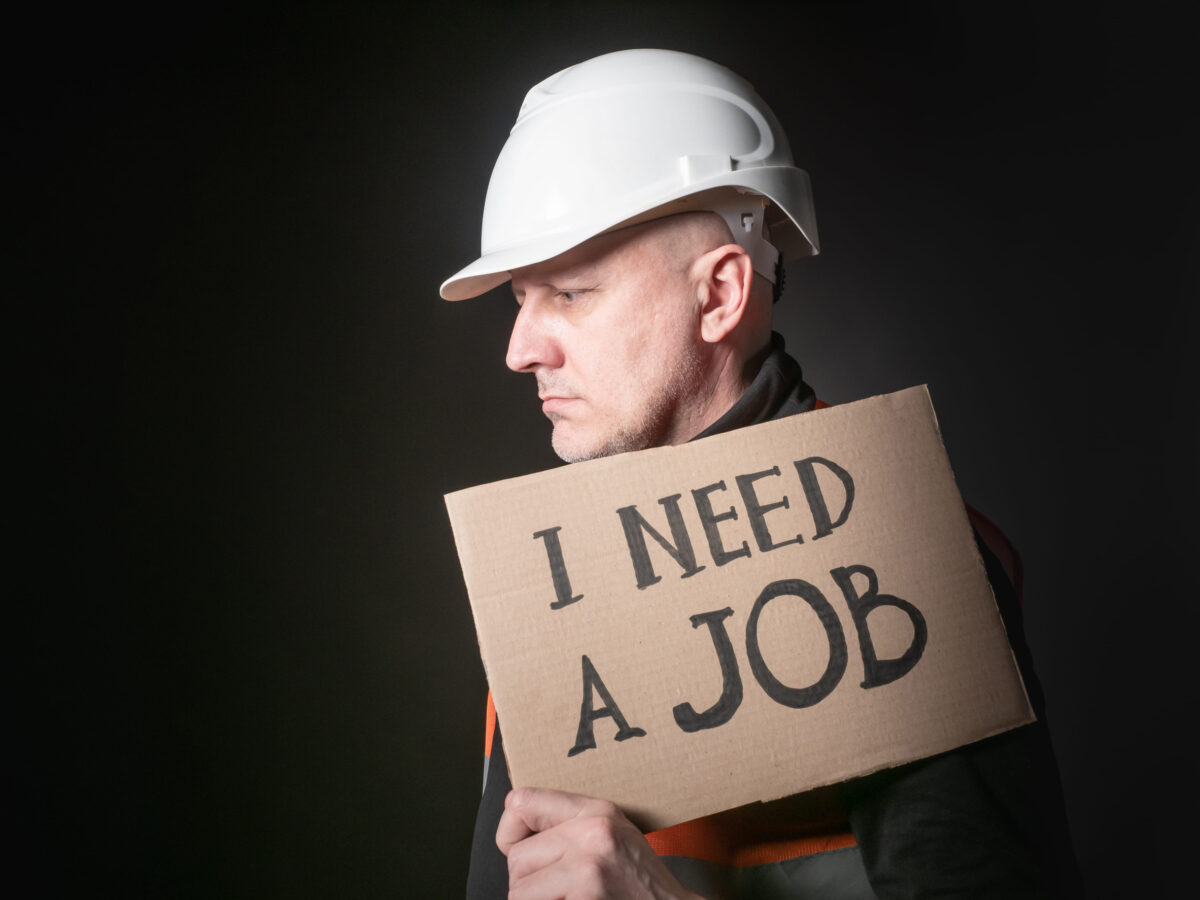 Man is looking for work. Inscription I need a job on the poster. Man in a builder helmet on a dark background. Concept - appeal builder to unemployment office. Engineer in job search. Sad. Upset