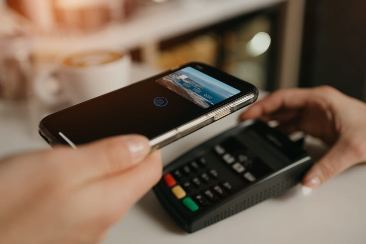The Psychology Behind Digital Tipping: Tap-to-Tip Screens Are Changing Guest Behavior 1 A girl paying for her latte with a smartphone by contactless PAY PASS technology in a cafe. A female barista holds out a terminal for paying to a client in a coffee shop.