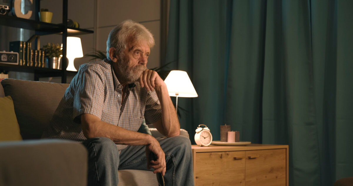 Senior man relaxing at home at night, he is sitting on the sofa and watching an interesting TV show