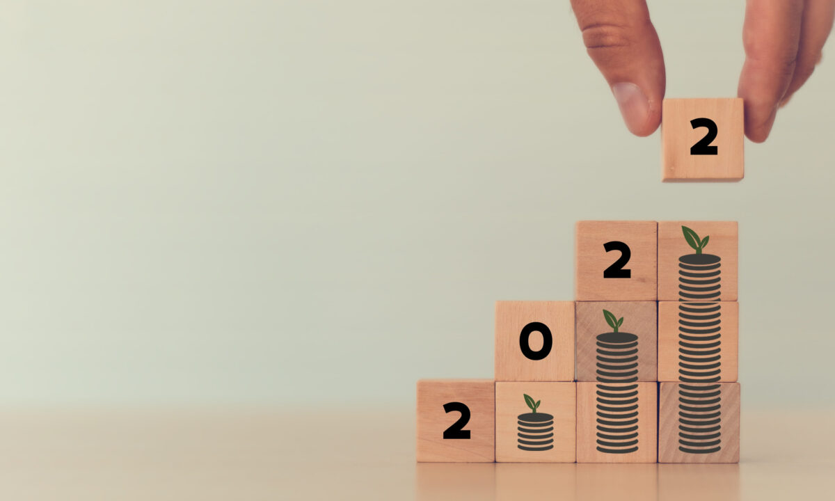 Financial growth concept in 2022. Close up hand arranging wooden cubes stacking '2022' standing on growth of coin stacking. White background and copy space. Financial and saving money growth banner.