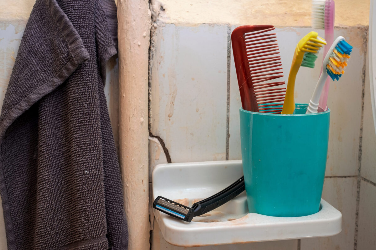 closeup of a comb and toothbrushes against cracked bathroom wall