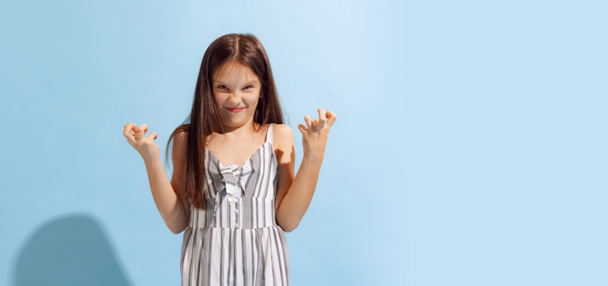 Annoyed school-age girl, kid in summer clothes posing isolated on light blue background. Concept of children emotions, fashion, beauty, school and ad