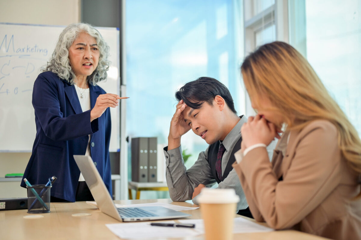 Stressed and upset Asian businesspeople receiving complaints from their boss during a meeting, feeling tired from an aggressive boss and an unfriendly office environment.