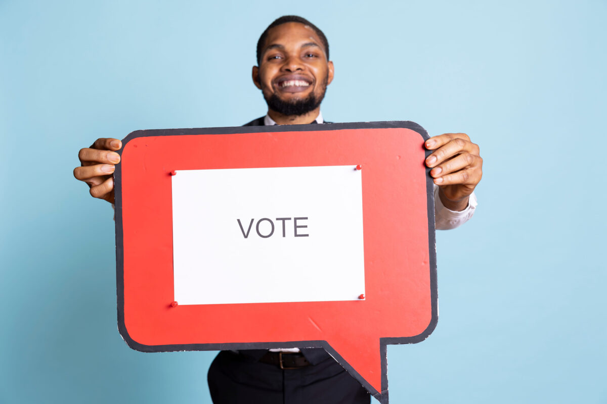 Hotel concierge holding a speech bubble with the message, urging people to get interested in politics on camera. Skilled bellhop with suit and tie showing an icon.