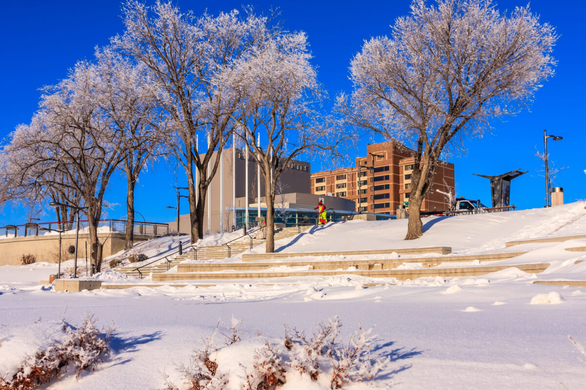 The 10 Best and Worst States for Having Kids, and Why Some “Affordable” Places Are Misleading 2 A snowy park with a building in the background. A man is walking on the snow. The sky is blue and clear