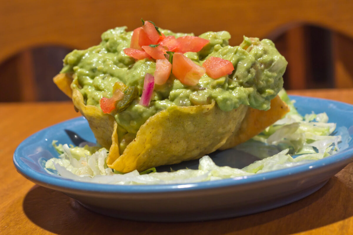 Mexican Guacamole dip with diced tomatoes in a crunchy tortilla bowl
