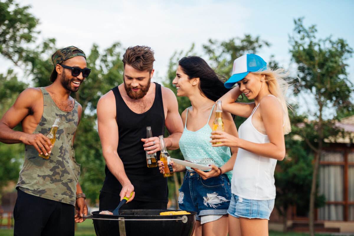 Group of happy young people standing and frying meet on barbeque grill outdoors