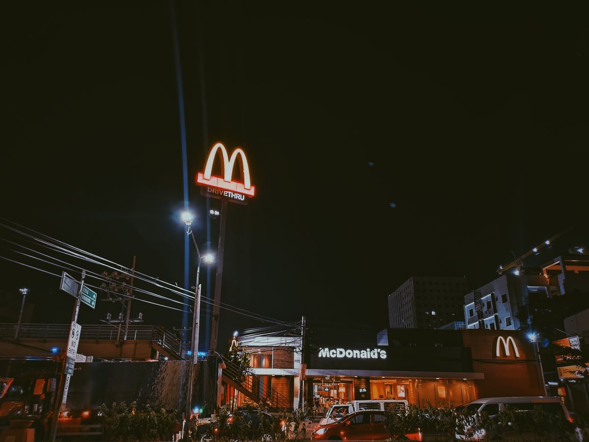 A brightly lit McDonald's restaurant in a city setting during nighttime, showcasing neon signage.