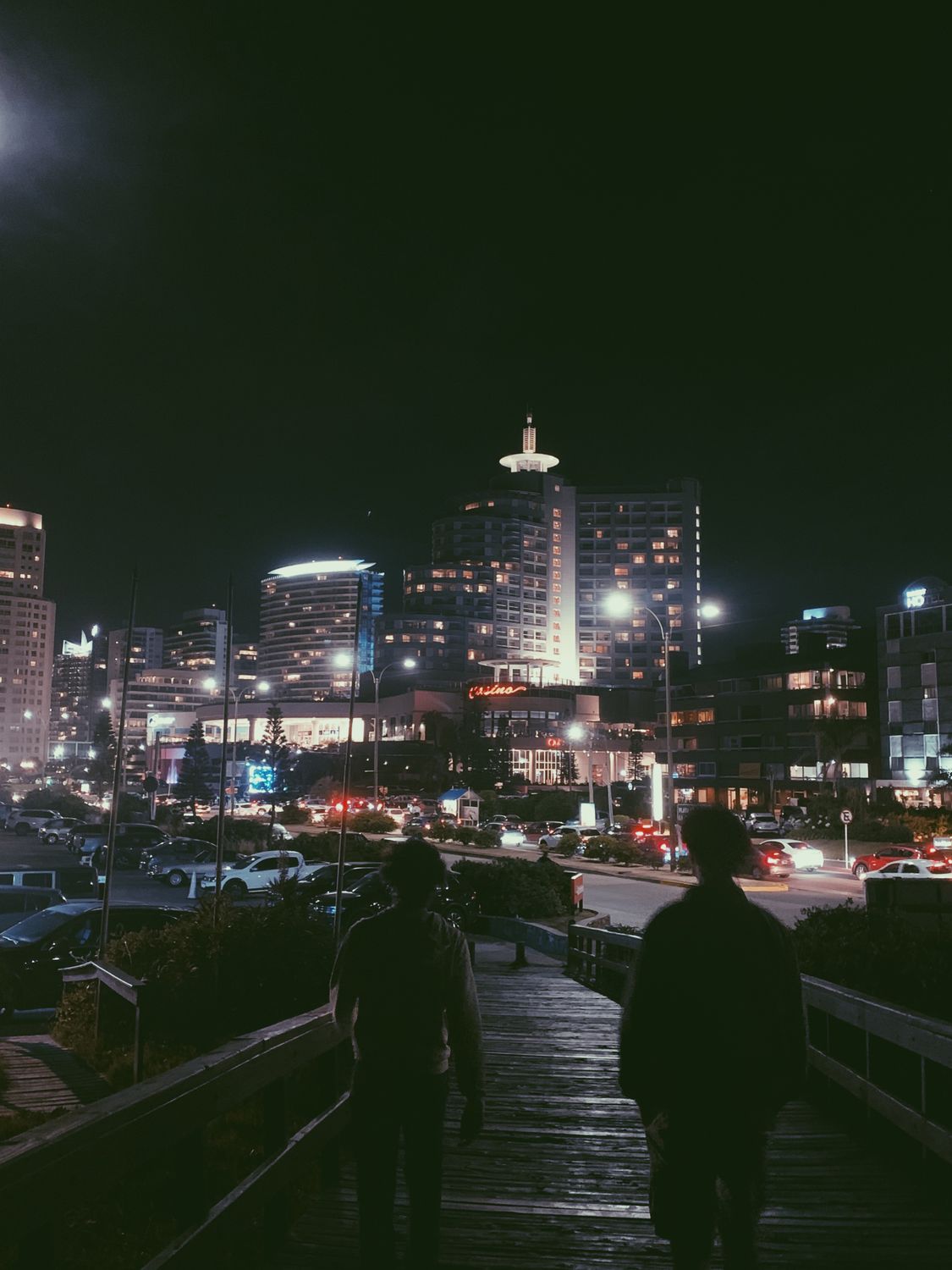 A bustling city street at night with illuminated buildings and people walking.