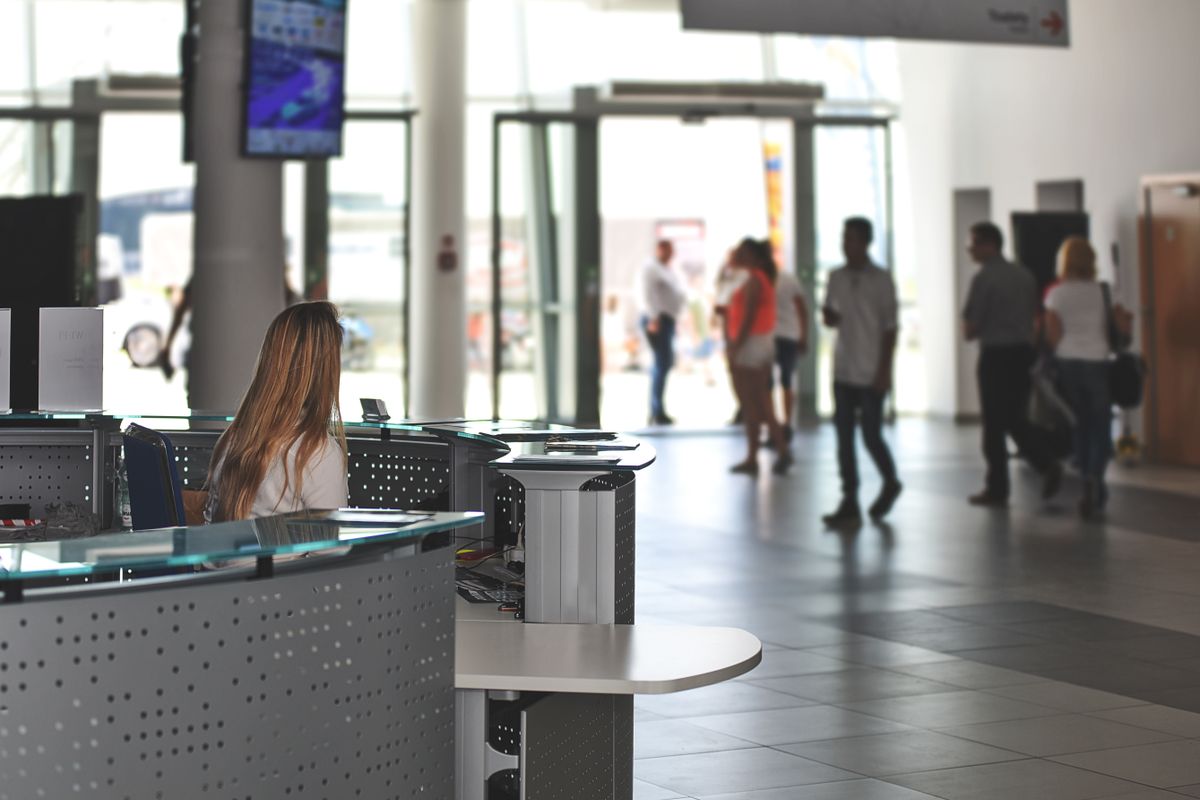The Commute Is Back, But Workers Are Not Going Back to the Old Office Life 3 A bustling office reception area with people walking and a receptionist at a modern desk.