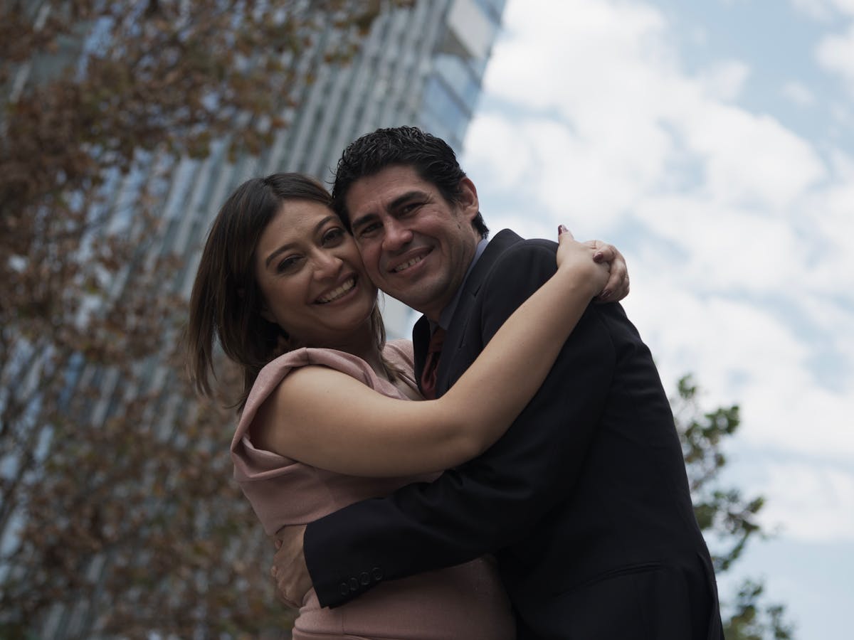 A cheerful couple hugging outdoors against a city skyscraper backdrop, conveying love and happiness.