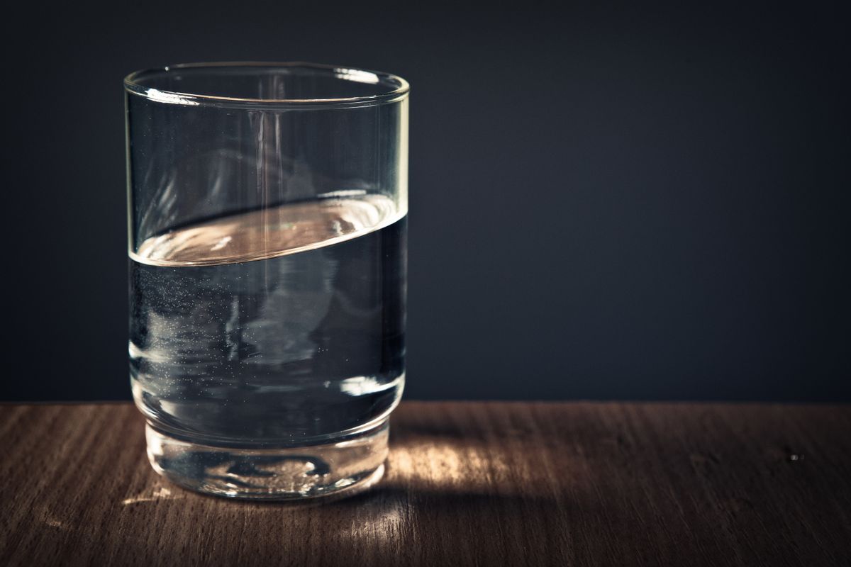 Brutally Relatable Things That Take Over ADHD Homes 3 A clear glass of water sitting on a wooden table against a dark background.
