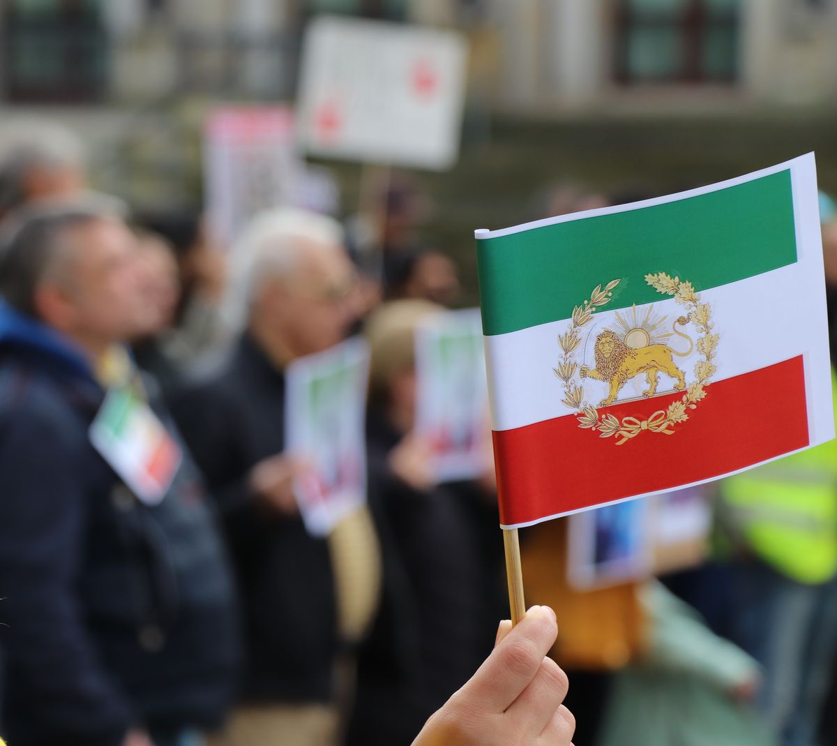 Ed Markey Calls for Trump Removal After Iran Threats Spark New Debate Over War Powers and International Law 2 A close-up of a hand holding the Iranian flag with a blurred crowd in the background.