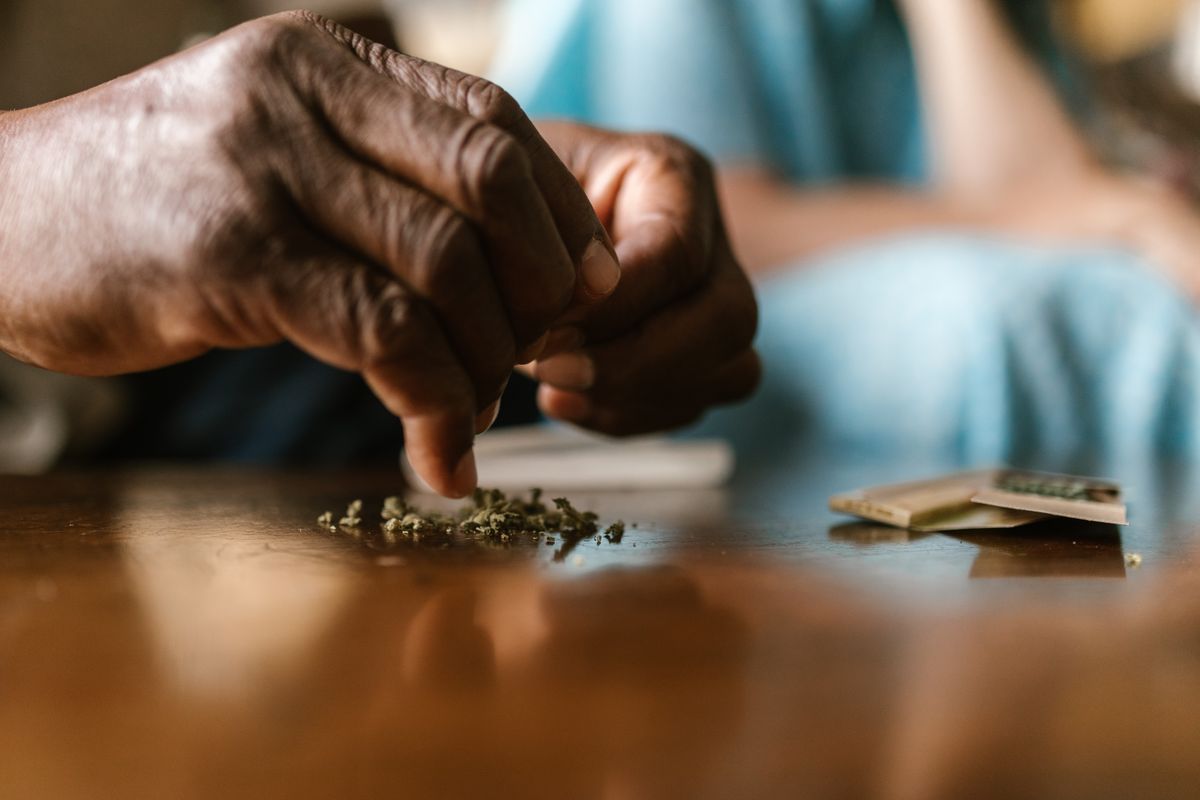 A close-up of hands skillfully rolling organic cannabis on a wooden table.