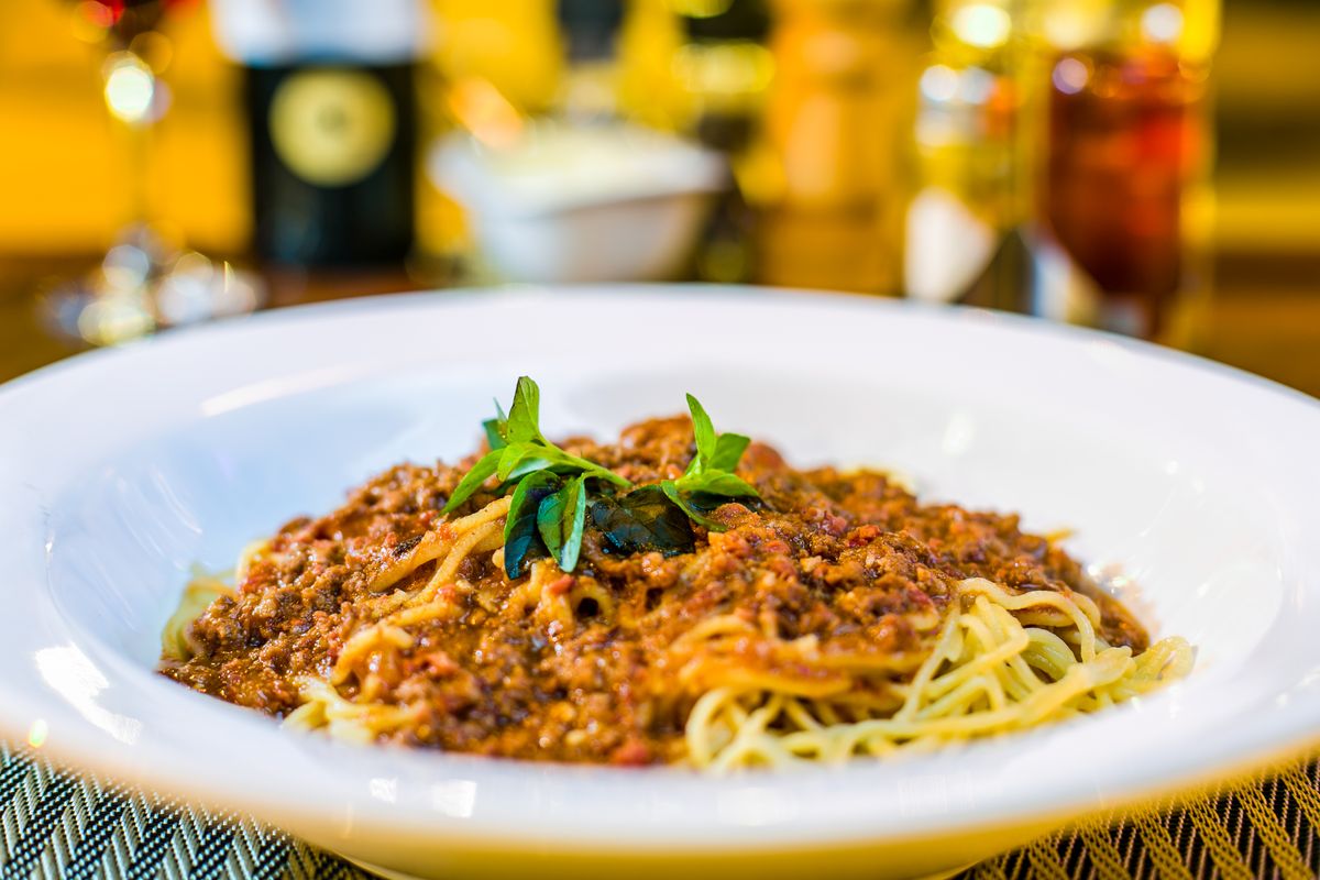 8 Weight Loss Killers Hiding In Your Daily Diet 2 A close-up of spaghetti Bolognese topped with fresh basil in a restaurant setting.
