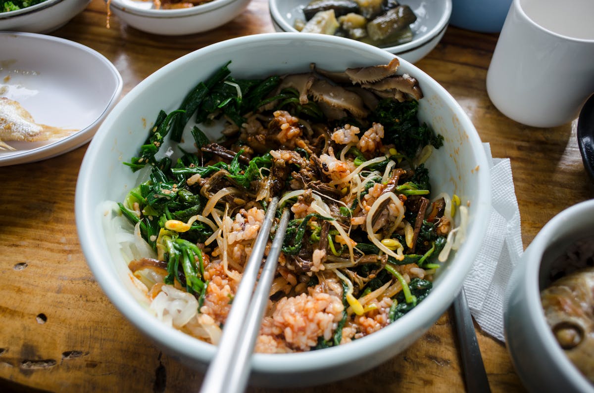 7 Hidden Dangers of Eating Food Directly from the Fridge 1 A colorful Korean bibimbap bowl filled with mixed vegetables, rice, and mushrooms in a close-up shot.