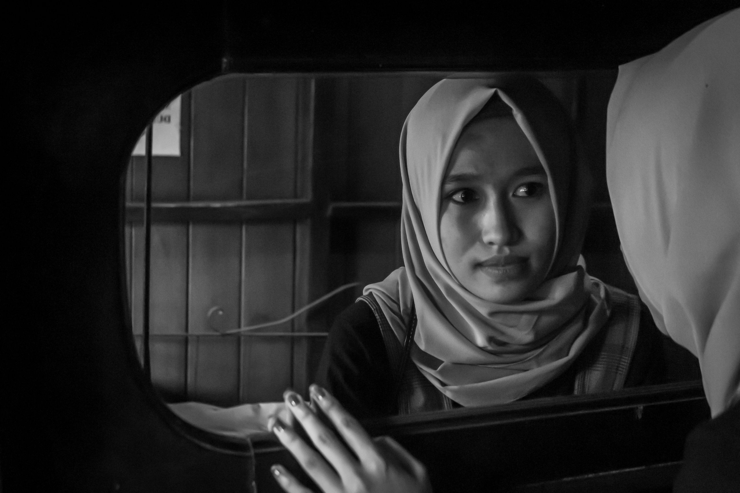 A contemplative black and white portrait of a woman wearing a hijab, gazing into a mirror.