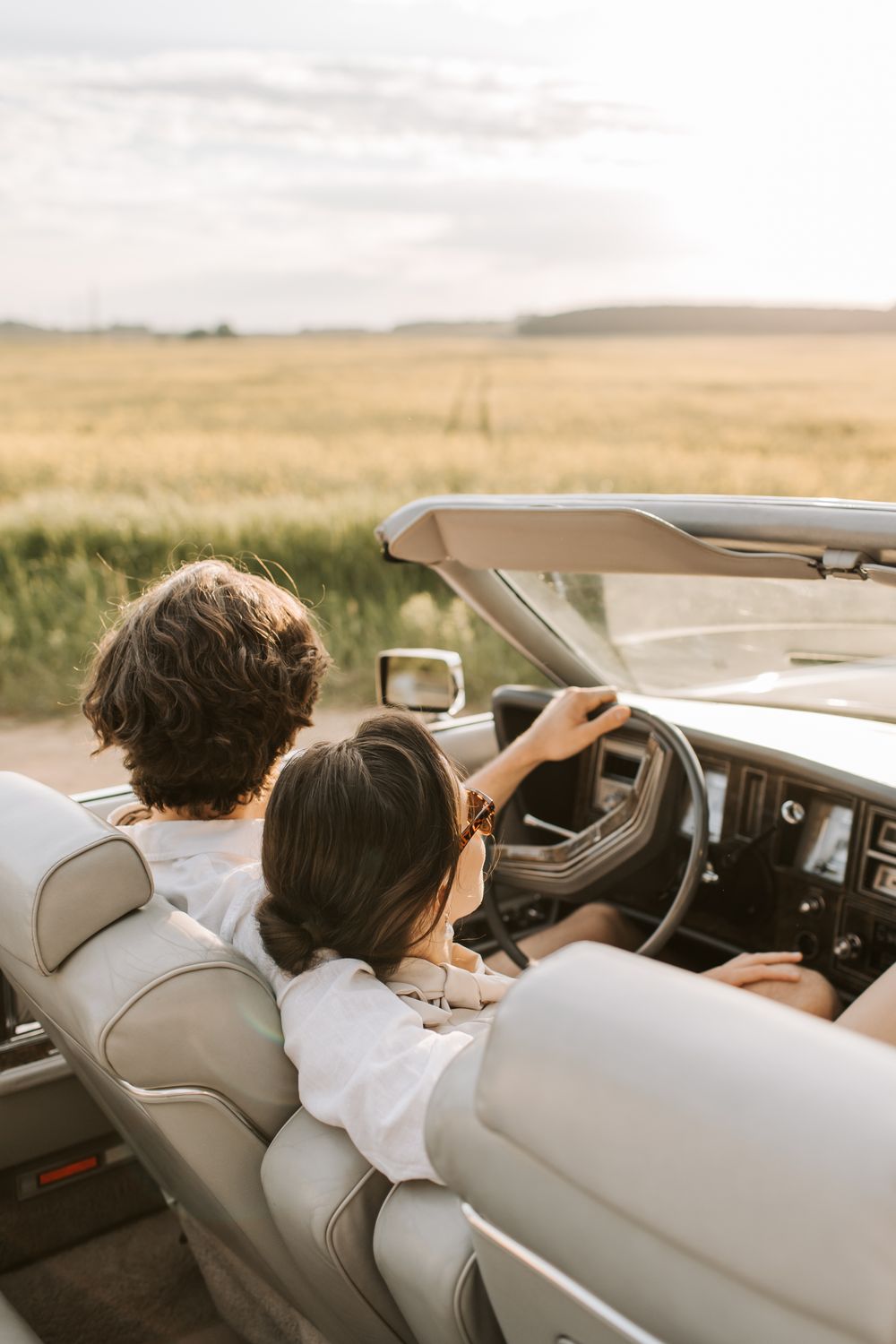 A couple enjoys a romantic drive through the countryside in a convertible car during the day.