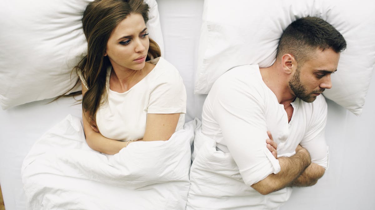 10 Shocking Reasons Good Relationships Fall Apart 2 A couple in bed, facing away with tense expressions, suggesting conflict.