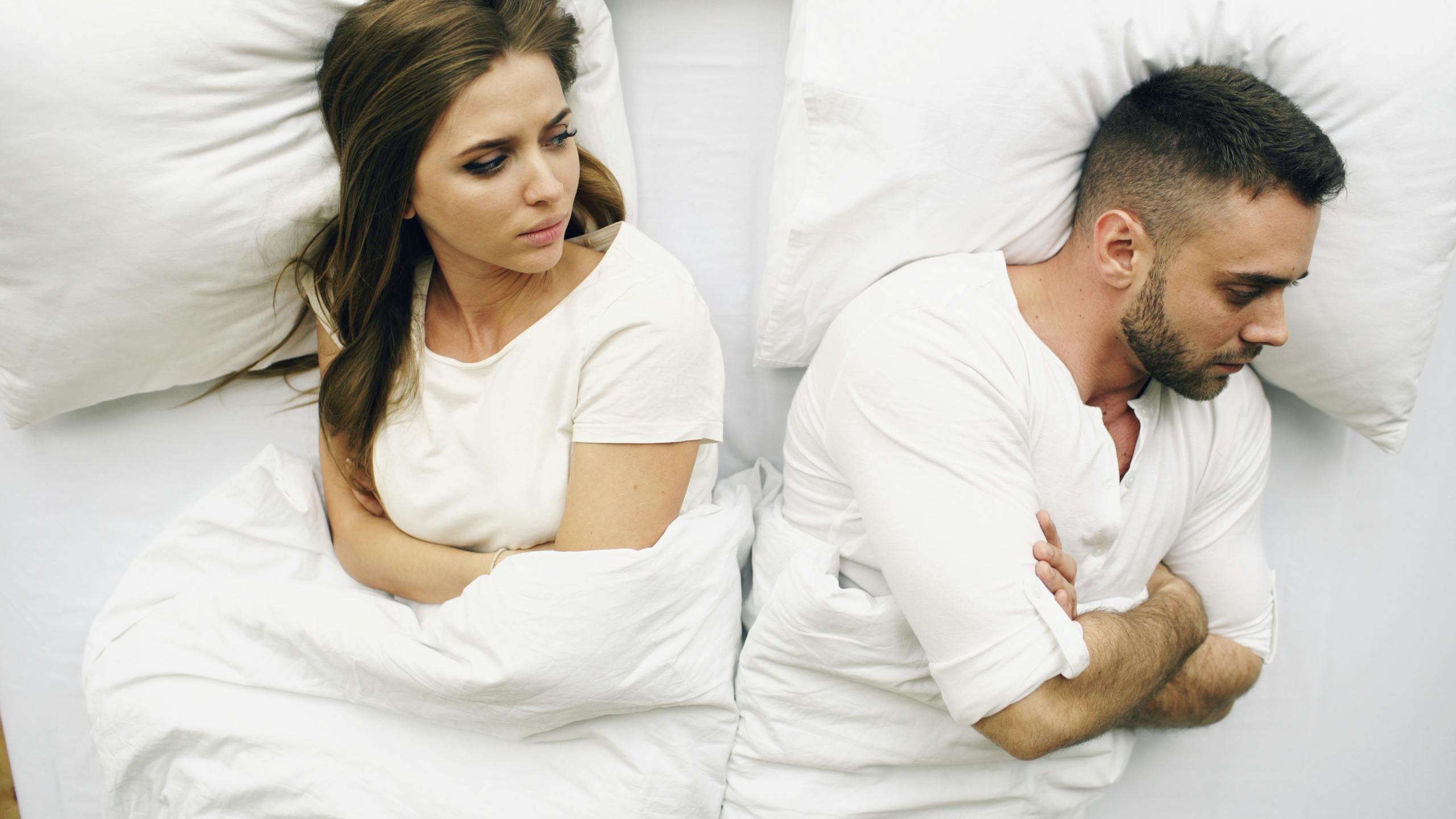 11 Small Marriage Mistakes That Quietly Push Women Away 3 A couple in bed, facing away with tense expressions, suggesting conflict.
