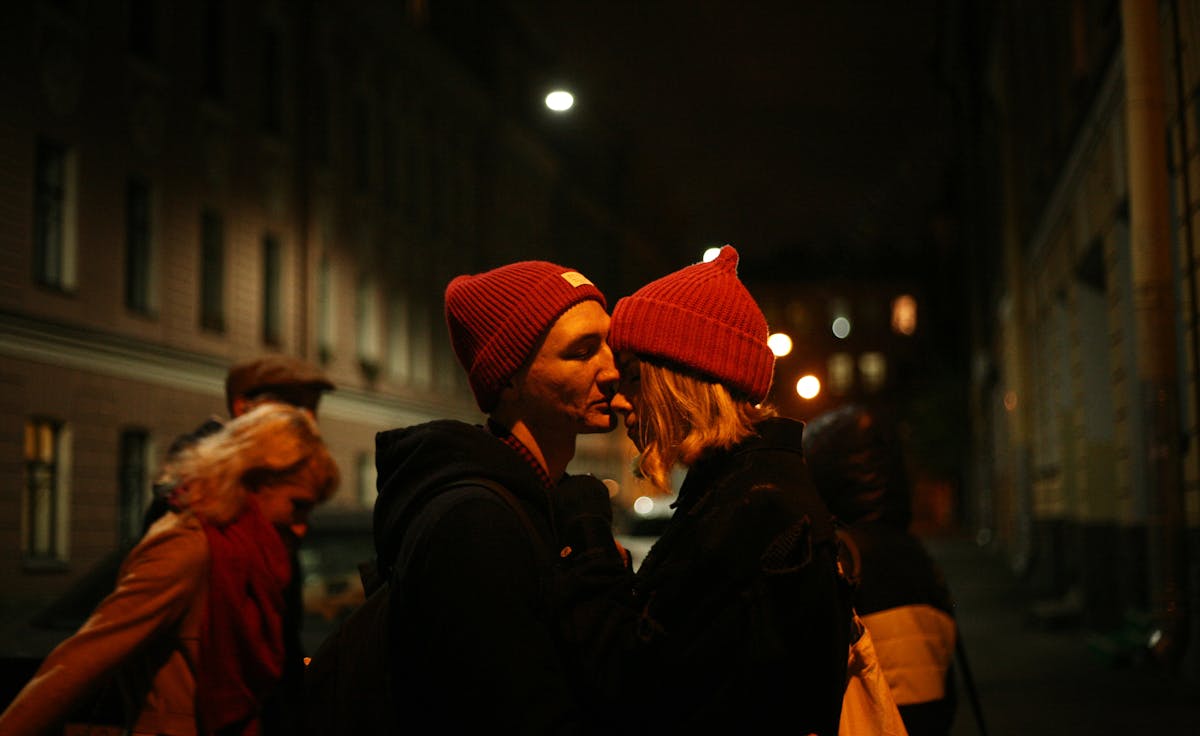 A couple shares a romantic kiss on a dimly lit street at night, embodying love and togetherness.