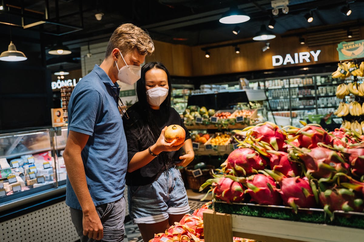 A couple wearing face masks shopping for fresh fruits at an indoor supermarket.
