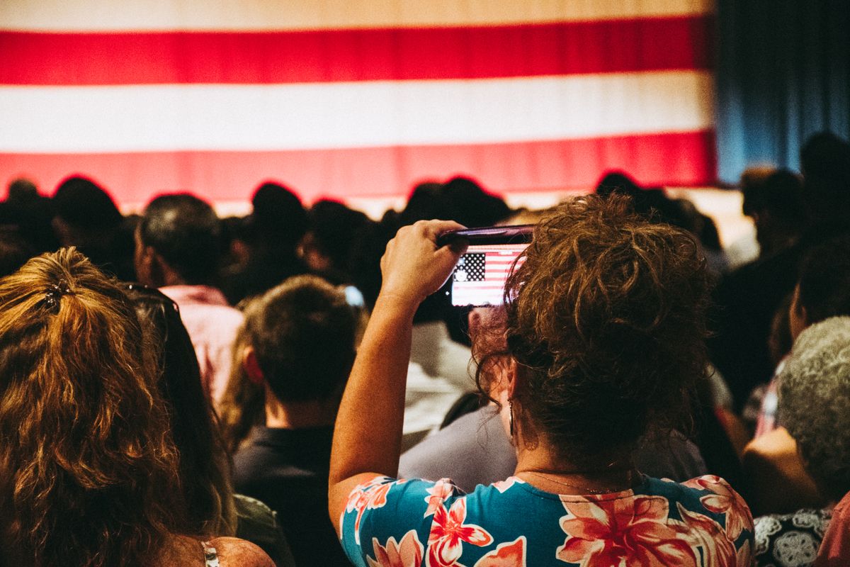 A crowd takes photos of an American flag at a busy indoor rally, encapsulating unity and patriotism.