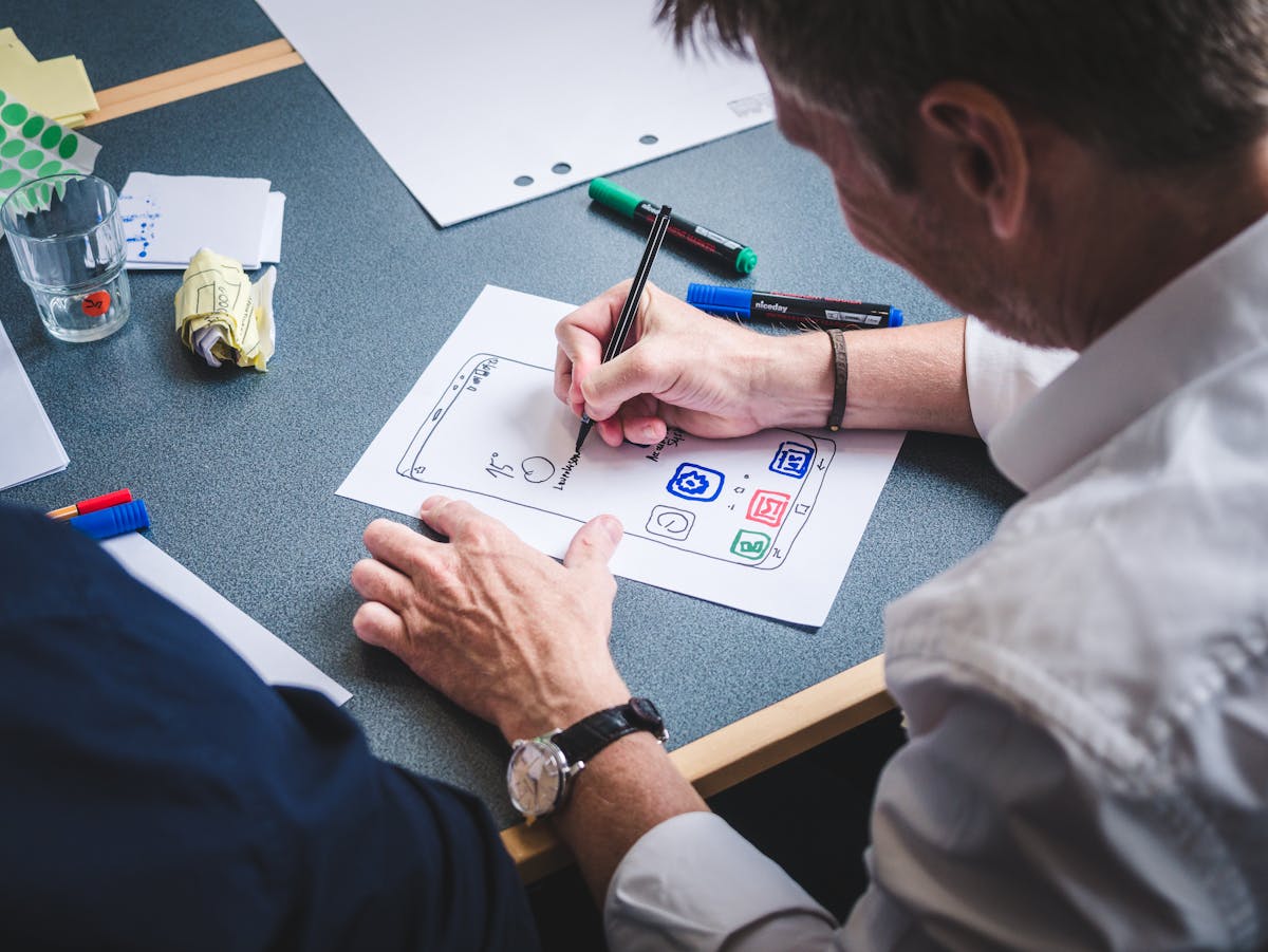 10 Job Skills You’re Ignoring That Are Killing Your Career 4 A designer sketches a mobile app prototype on paper at an office desk, focusing on creativity and design.