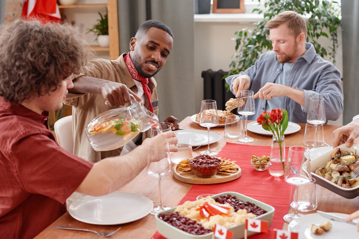 A diverse group enjoying a festive meal with beverages and Canadian-themed decor.