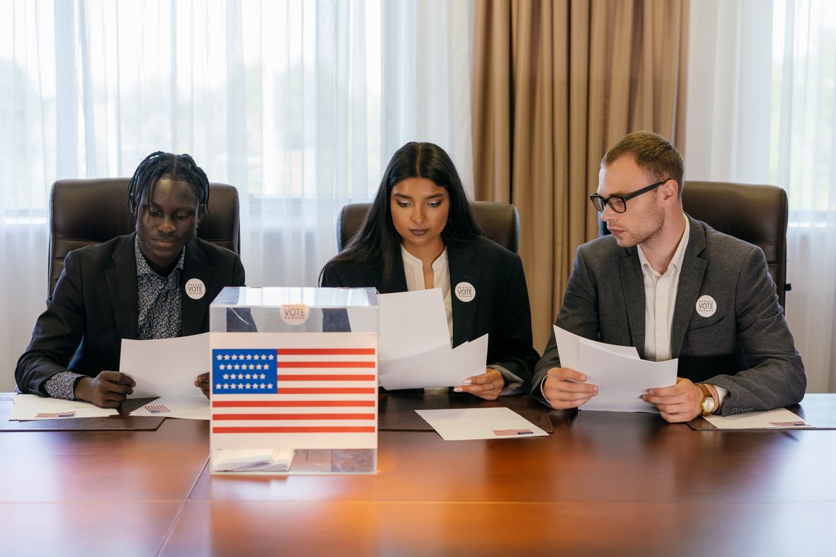 A diverse group of professionals examining papers near a voting box indoors.