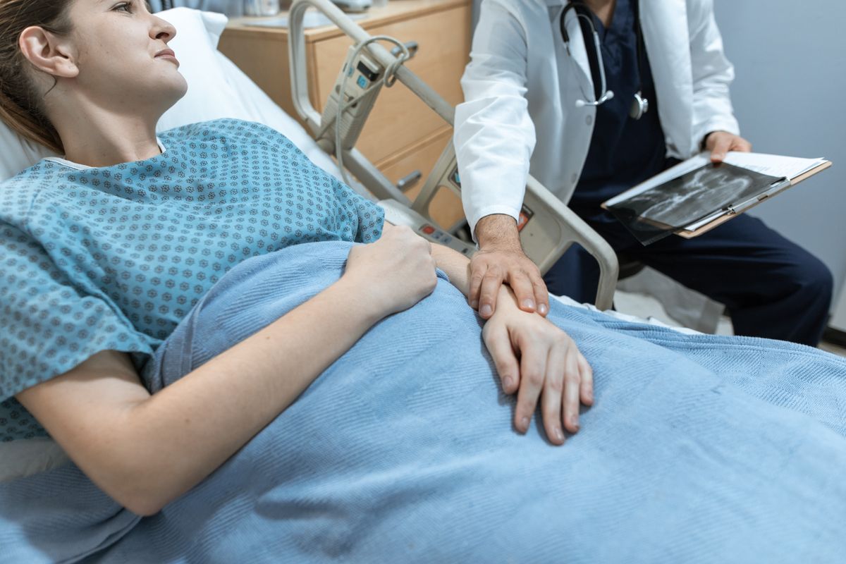 7 Concealed Illnesses Weakening Your Body Without Clear Symptoms 2 A doctor comforts a female patient in a hospital bed, holding her hand, with x-ray results.