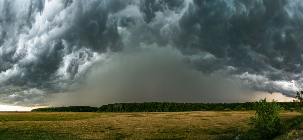 A dramatic thunderstorm rolls over a vast countryside field, creating an intense and moody atmosphere.