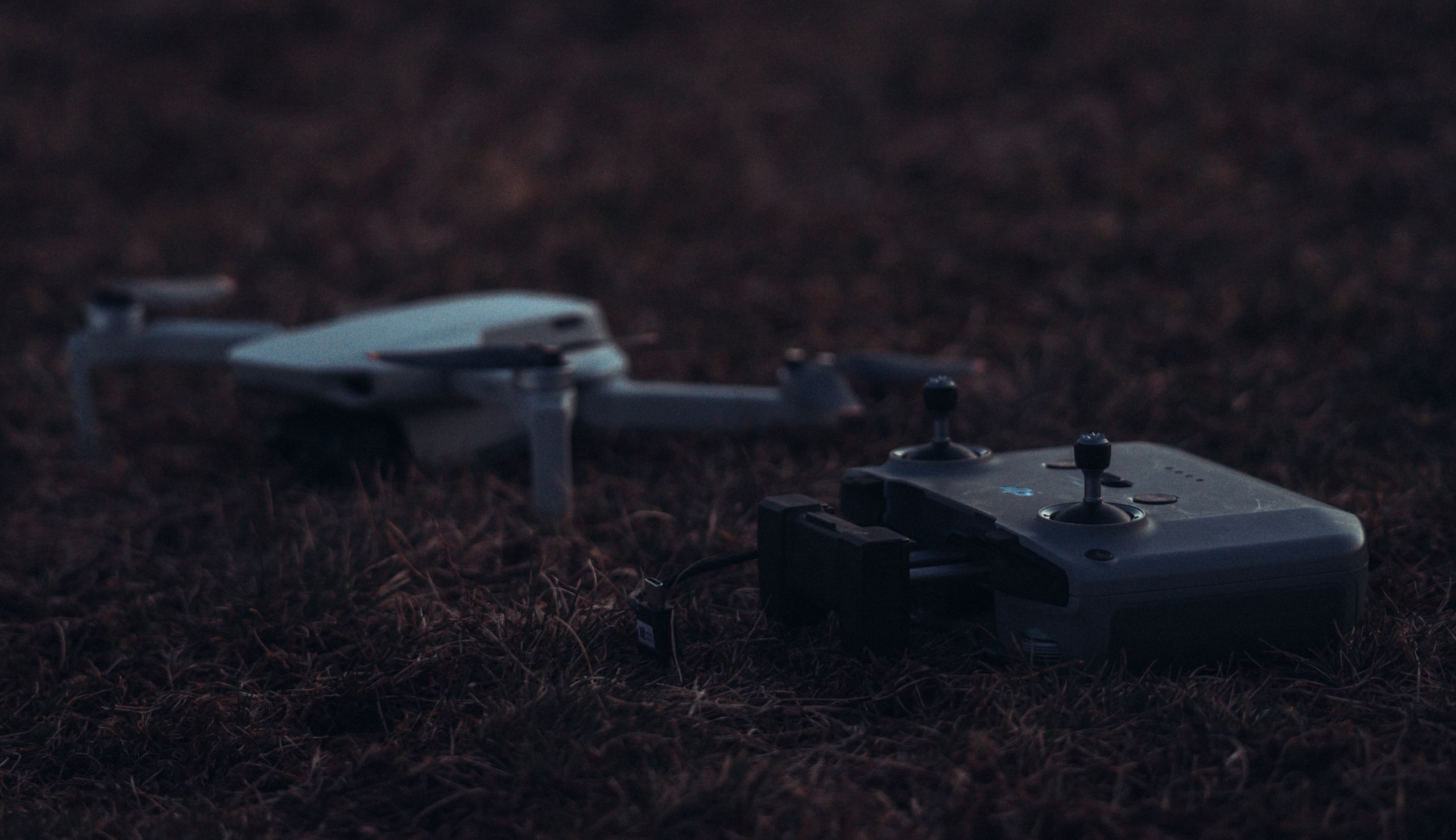A drone and controller resting on grass, captured at dusk with a calm atmosphere.
