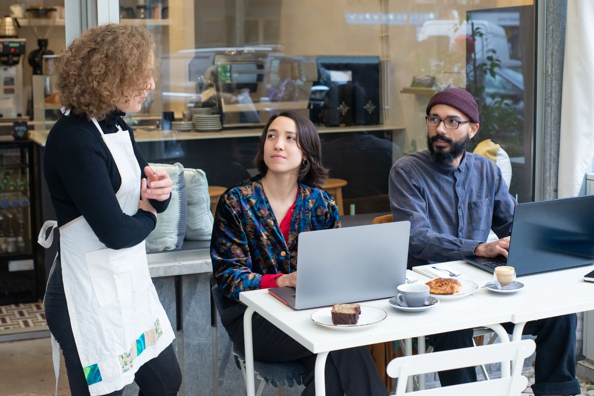 In Texas, a Local Tomball Kolache Café Is Going Viral With Its Affordable Menu 1 A dynamic outdoor café setting in Portugal with people working on laptops and a waitress serving.