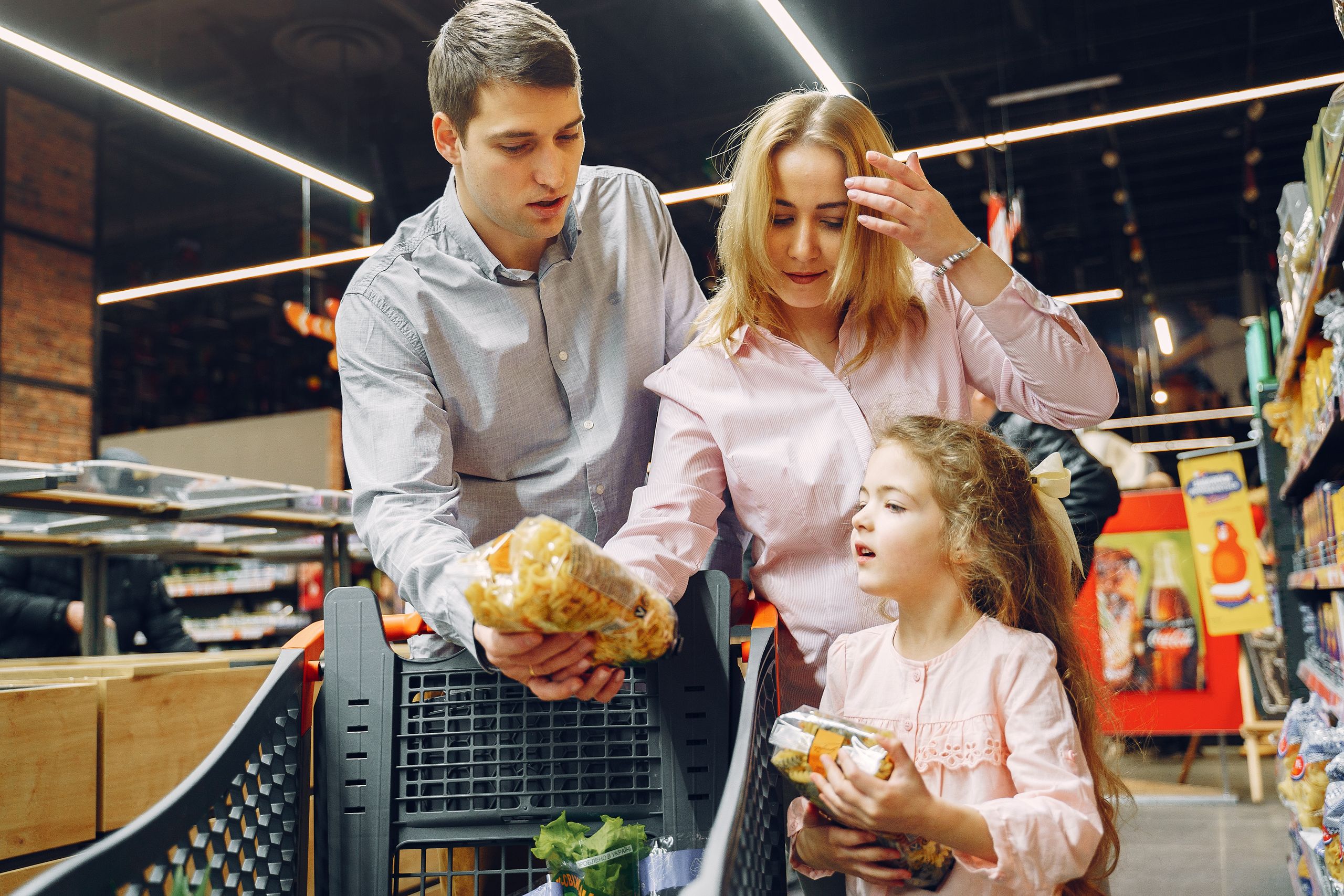 Americans Are Draining Savings to Buy Groceries as the Cost of Living Squeeze Deepens 2 A family enjoying shopping in a supermarket aisle, selecting groceries with a cart.