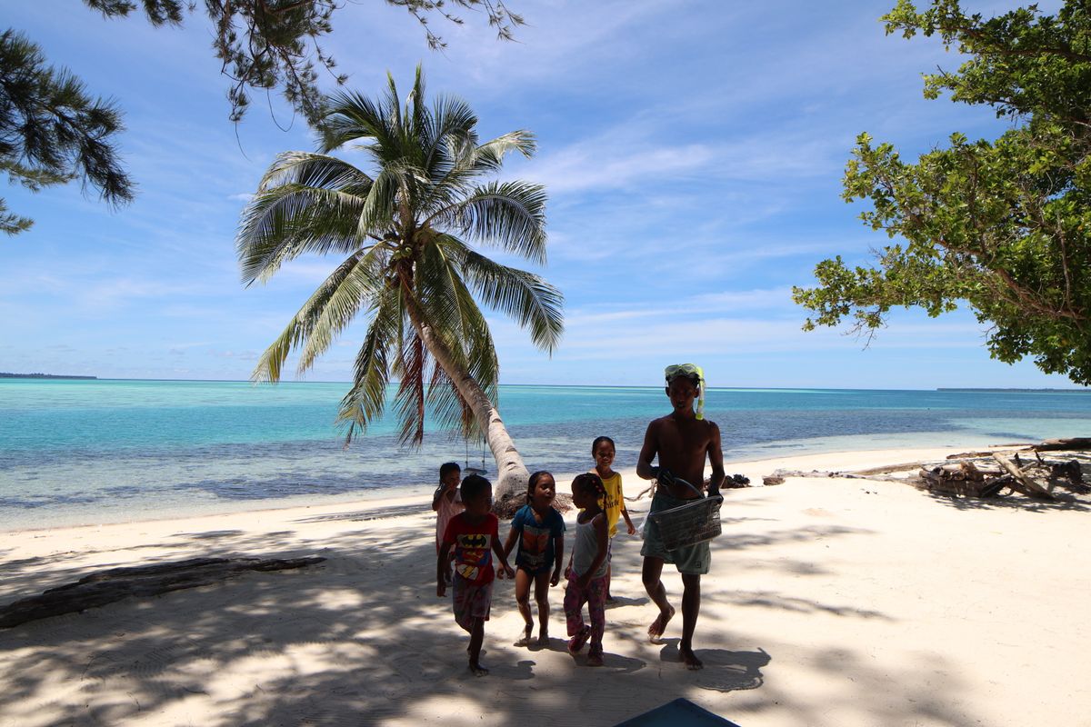 A group of children playing joyfully on a scenic tropical beach in Balabac, Philippines under clear blue skies.