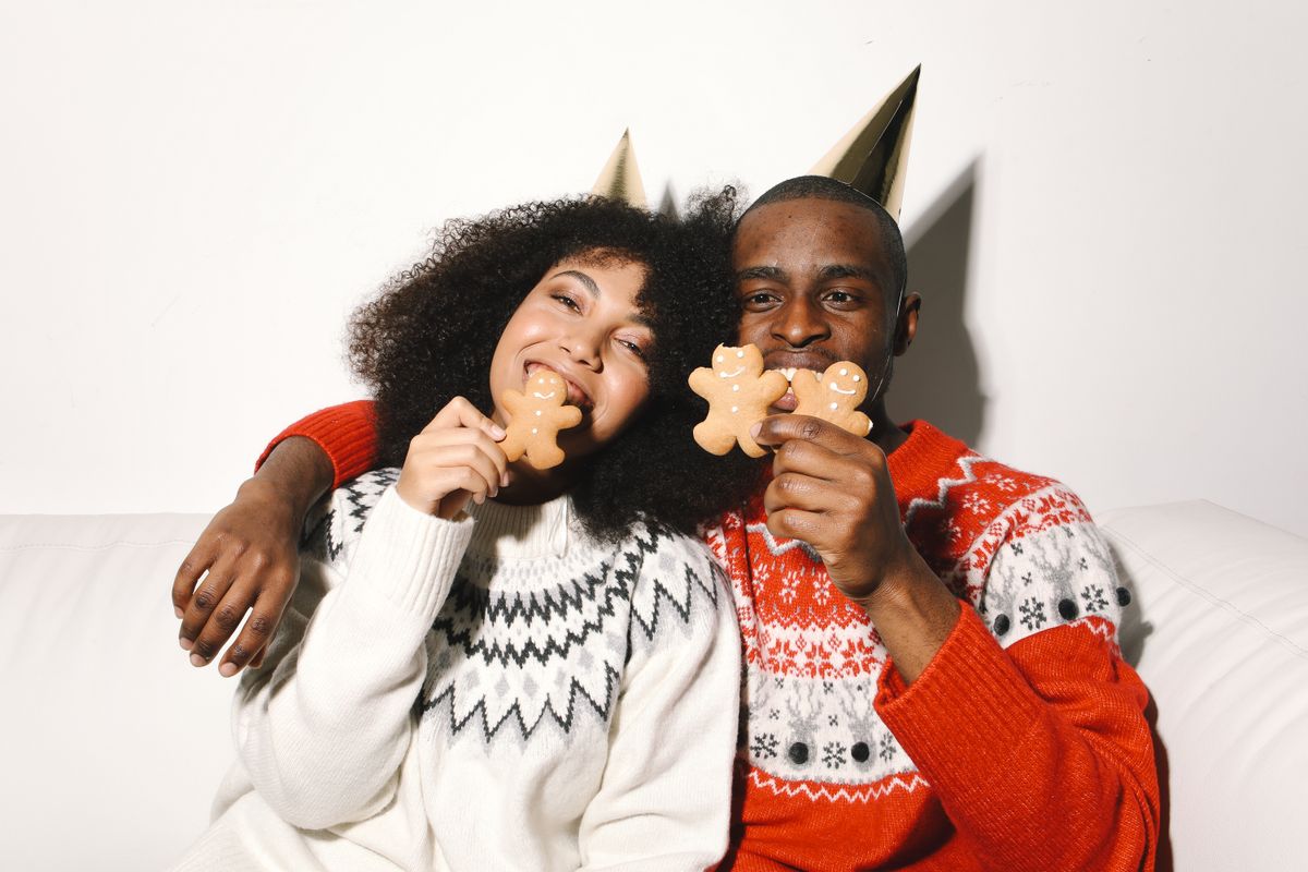 A happy couple in festive sweaters enjoying gingerbread cookies at a celebration.