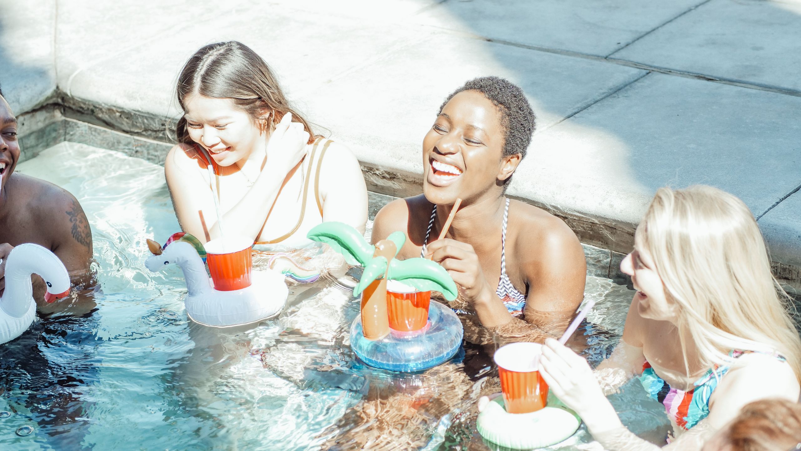 11 Reasons a Girls Trip Can Turn Into a Friendship Disaster 4 A joyful group of friends enjoying drinks and laughter at a sunny poolside party.