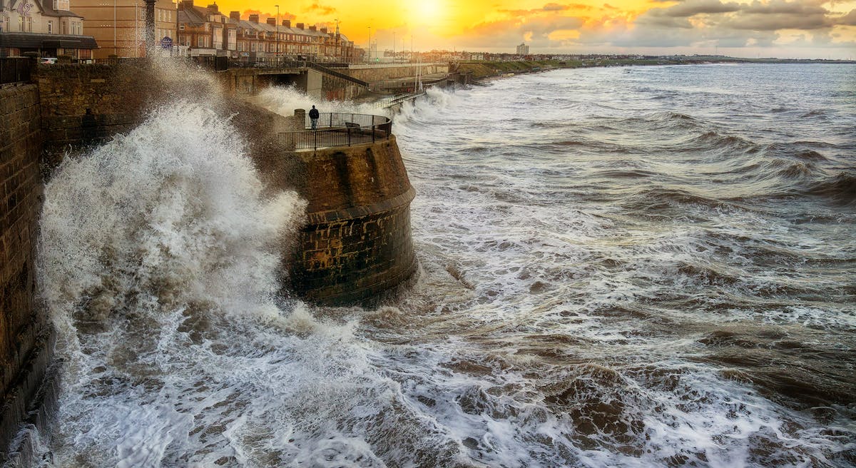 7 Hidden Dangers Along Europe’s Coasts Experts Say Could Unleash a Killer Wave 3 A lone figure stands by the sea as powerful waves crash against the coast at sunset.